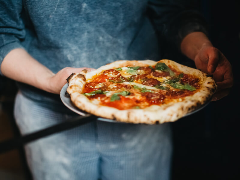 A close up of a person holding a handmade pizza