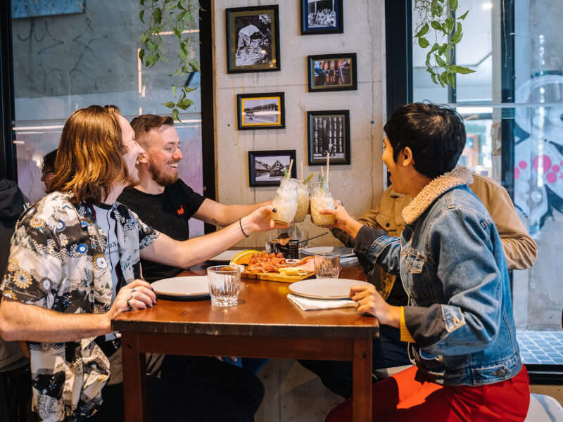 A group of men and women are sitting at a table, clinking glasses in a 'cheers' motion