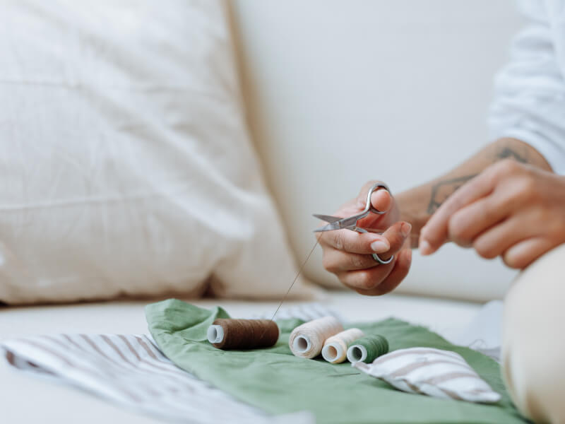 A person is cutting brown thread over a table covered in green fabric