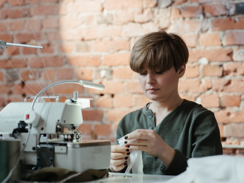A woman sits at a sewing machine, holding white fabric, ready to learn how to sew
