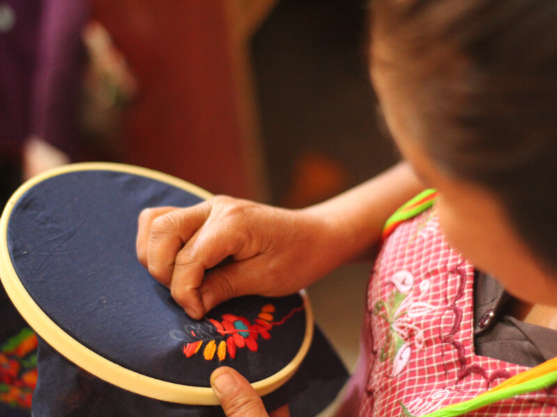 A close up of a person embroidering flowers onto dark blue fabric
