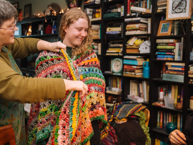 A woman is draped in a colourful crochet granny square blanket