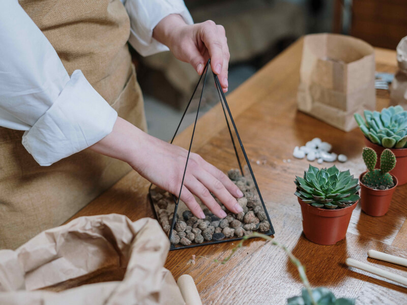A person adding stones to the bottom of a glass terrarium