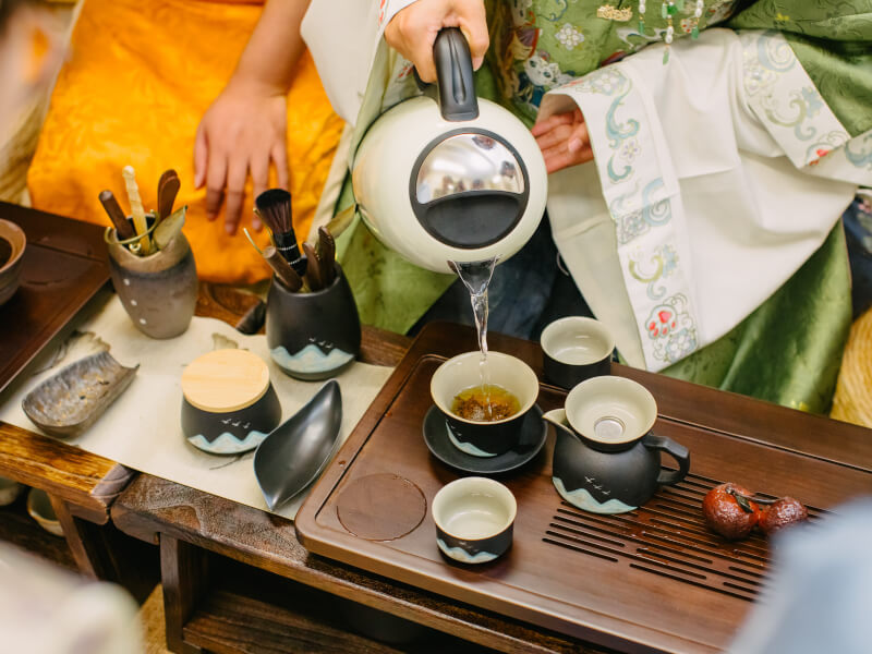 A close up of a person pouring water from a kettle into a teacup filled with tea leaves