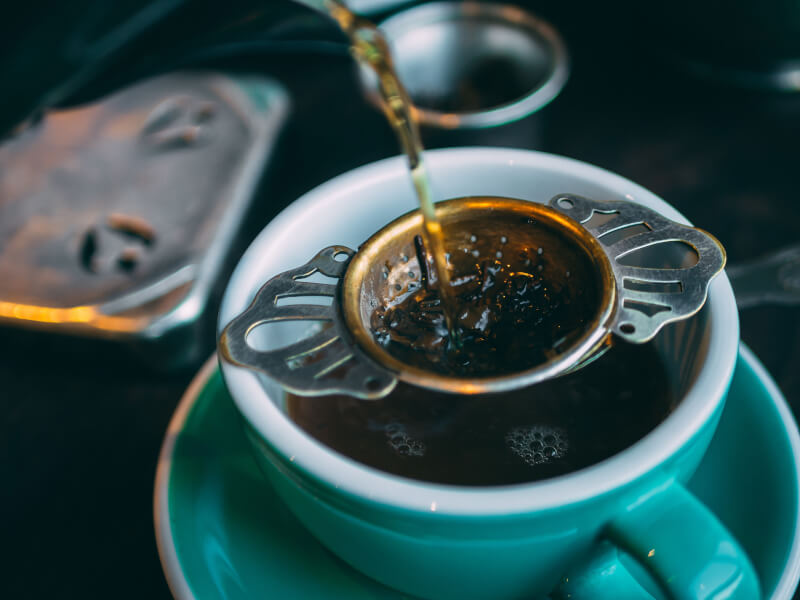Loose leaf tea being poured into blue cup and saucer using a strainer.
