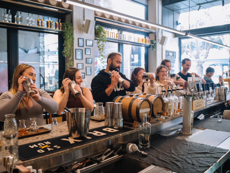 A group of people at a bar are making cocktails using silver cocktail shakers