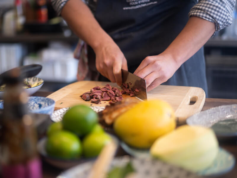 A person is chopping cooked steak on a wooden board