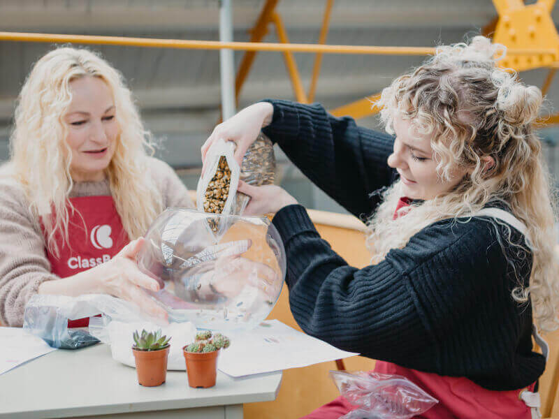Two women adding stones to a glass terrarium