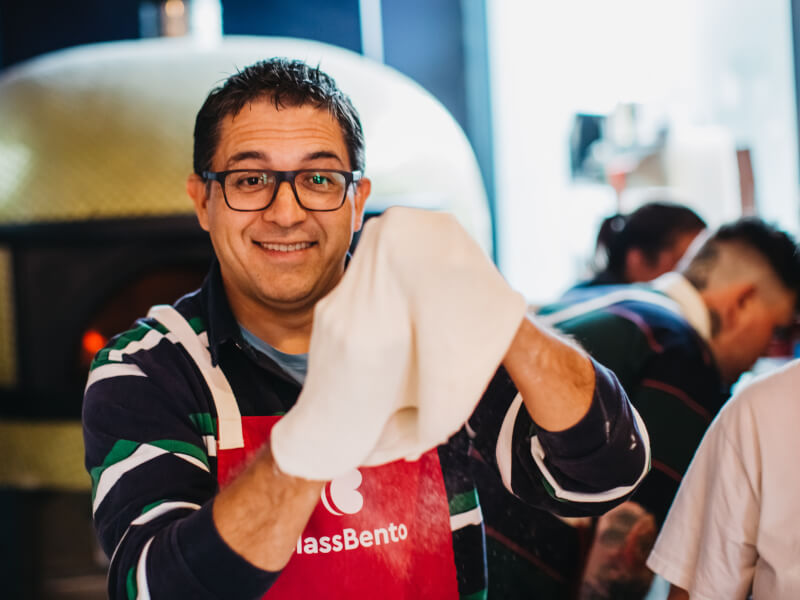 A smiling man holds up handmade pizza dough, ready to be topped