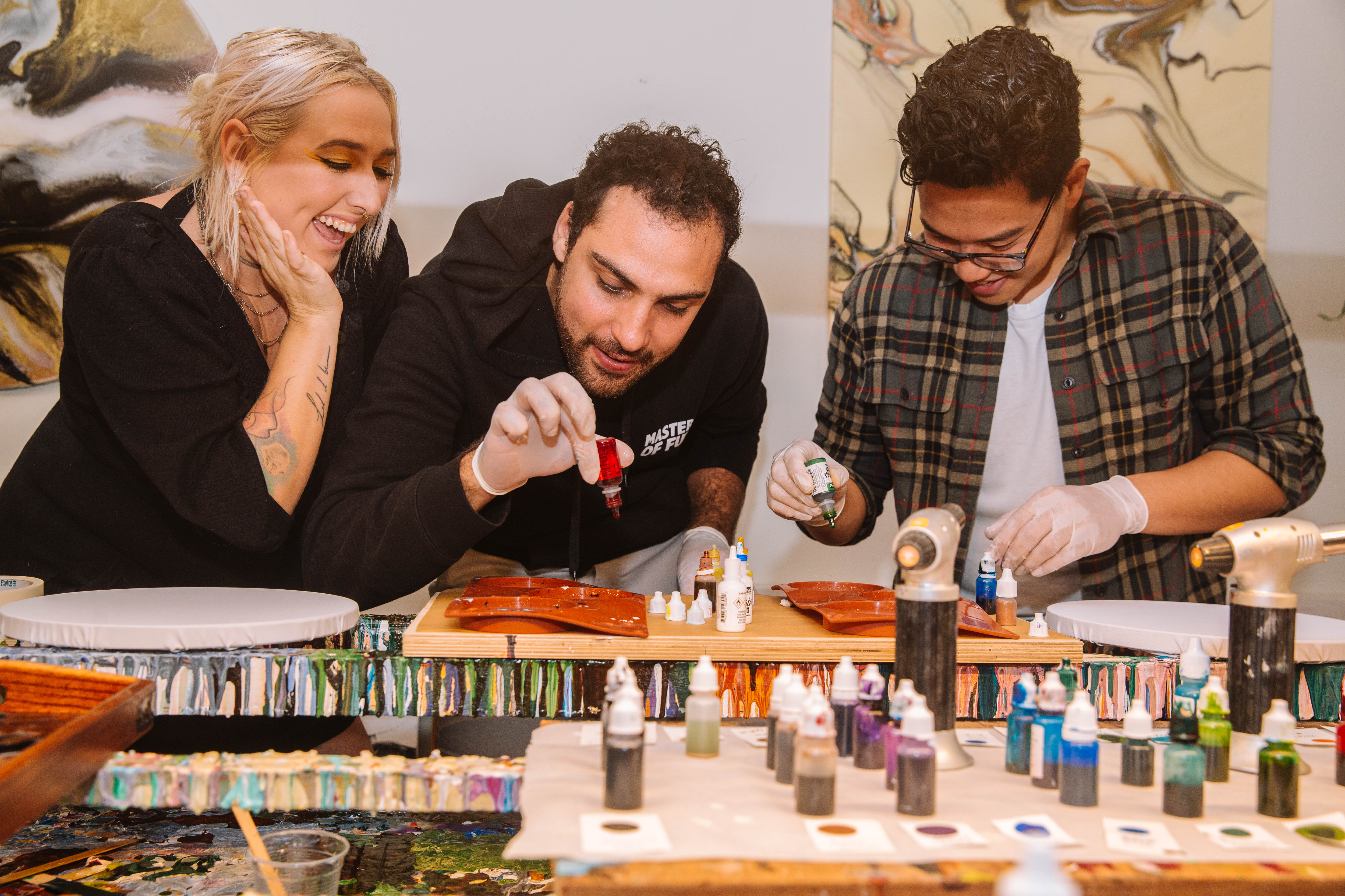 A woman is teaching two men how to create fluid art