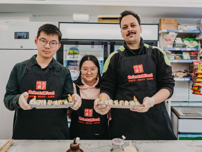 Three people are holding handmade sushi and smiling