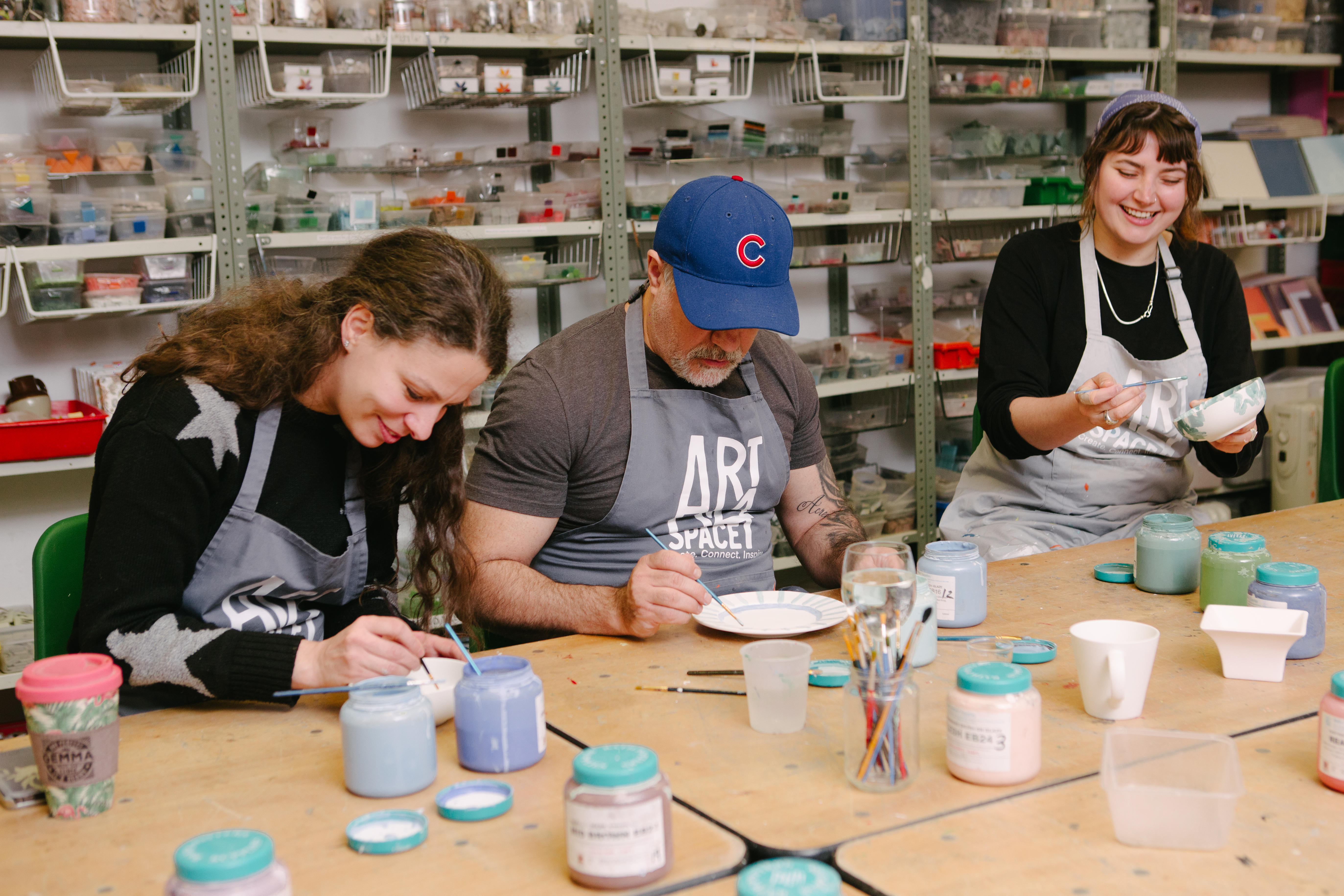 Three people are painting pottery in a studio