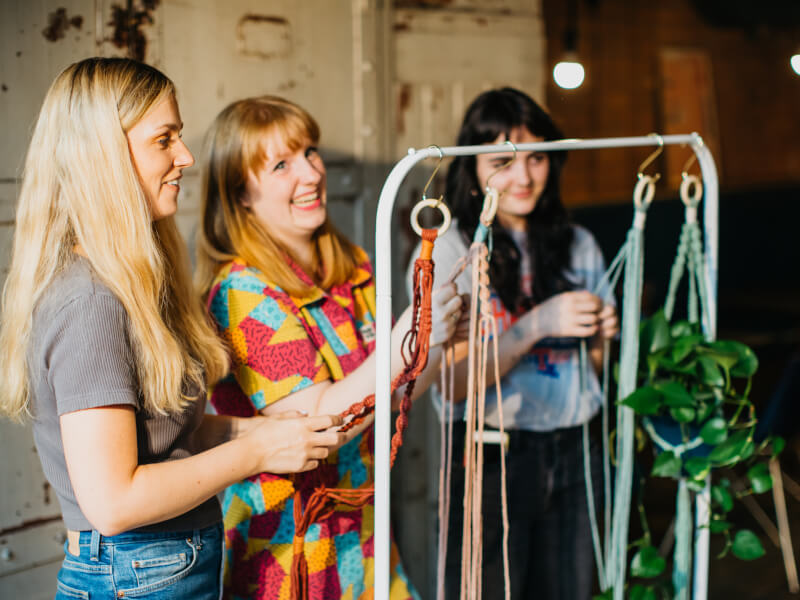 Three women are making macrame plant hangers in colourful cord