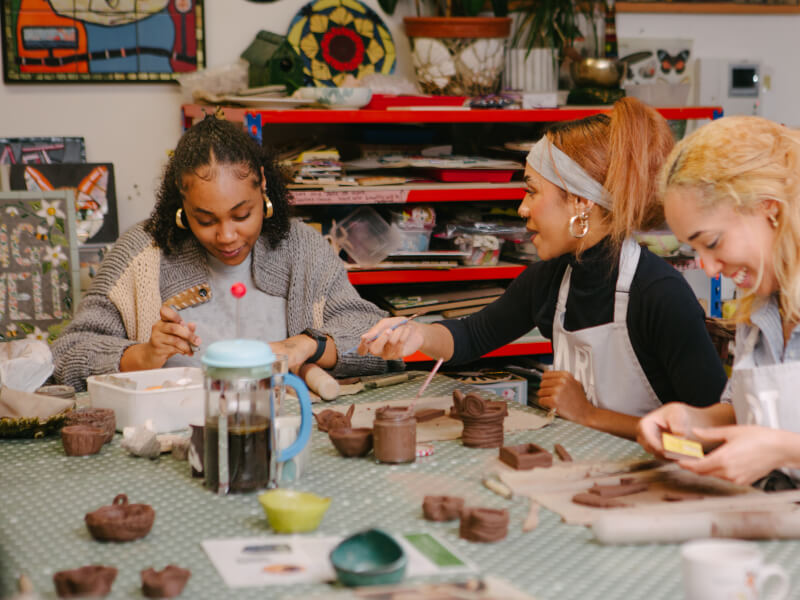 Three women handbuilding pottery and laughing