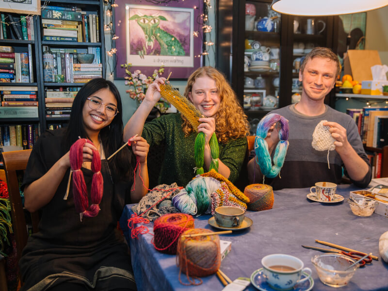 Three people crocheting in coloured yarn at a table