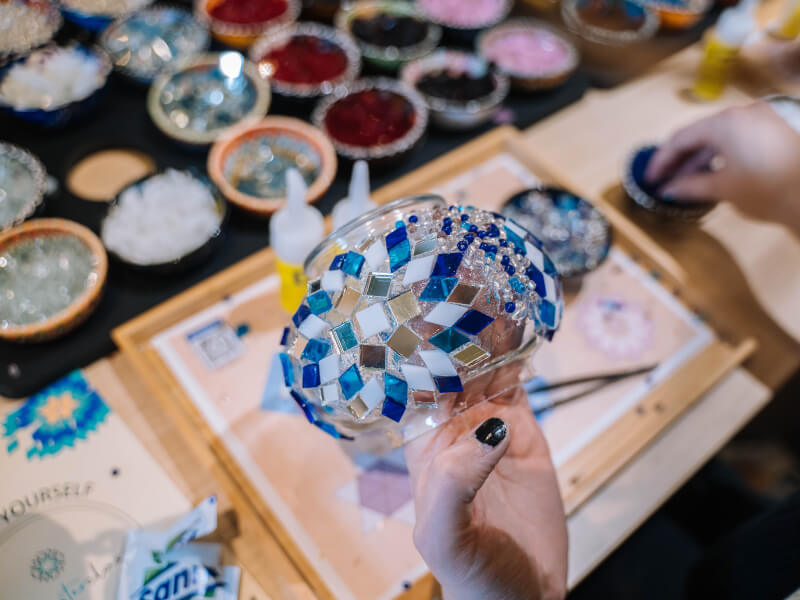 A close up shot of a person adding coloured glass tiles to a glass lampshade