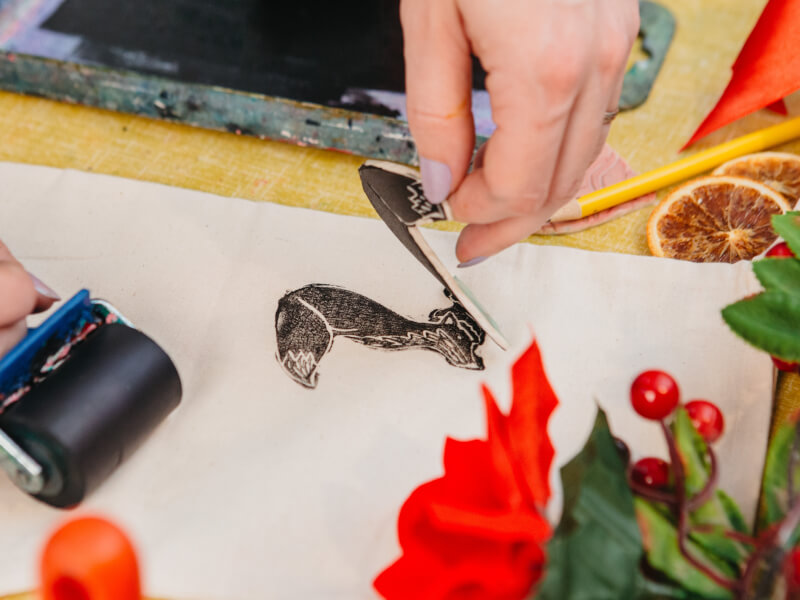 A close up of a person lifting a lino block off of a piece of fabric after printing an image on it