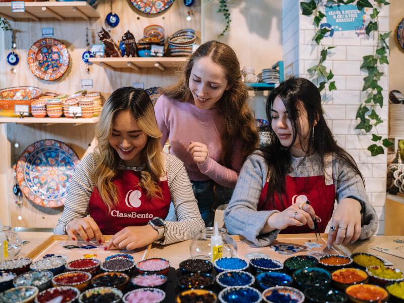 Three women smiling and using mosaic tiles in a mosaics class