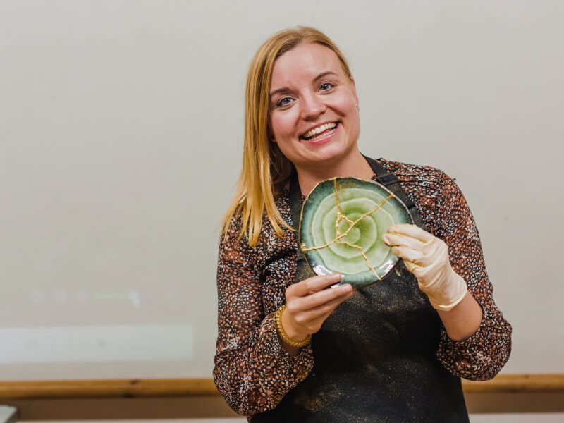 A woman smiling and holding up a kintsugi plate she's repaired herself
