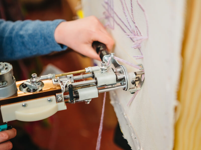 A close up of a person using a tufting gun with pink yarn