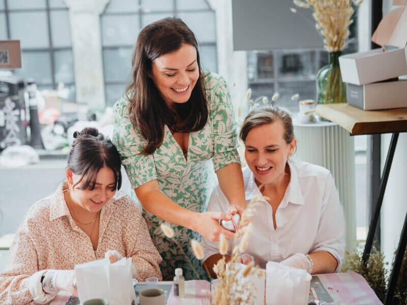 Two women are being taught to make aromatherapy rollerballs by a teacher