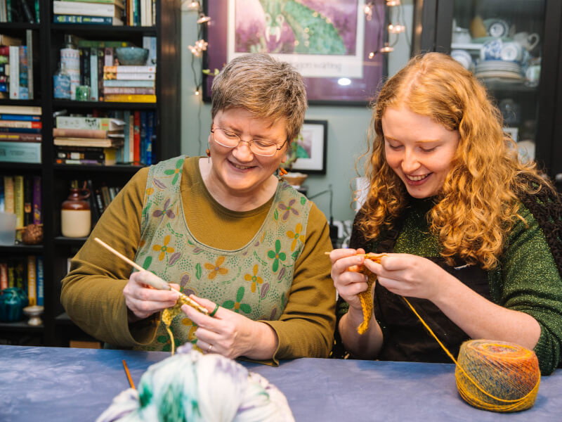 Two women sitting at a table crocheting with yellow yarn