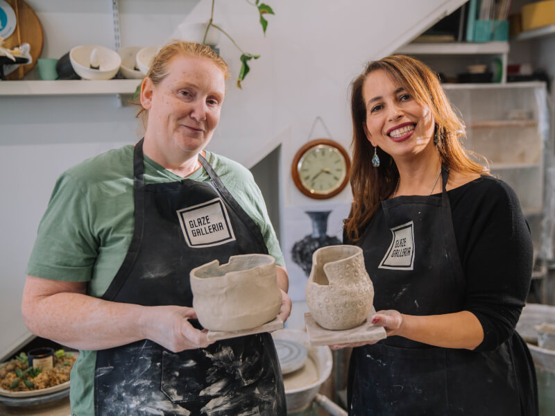 Two women are holding handmade sculpted clay pots