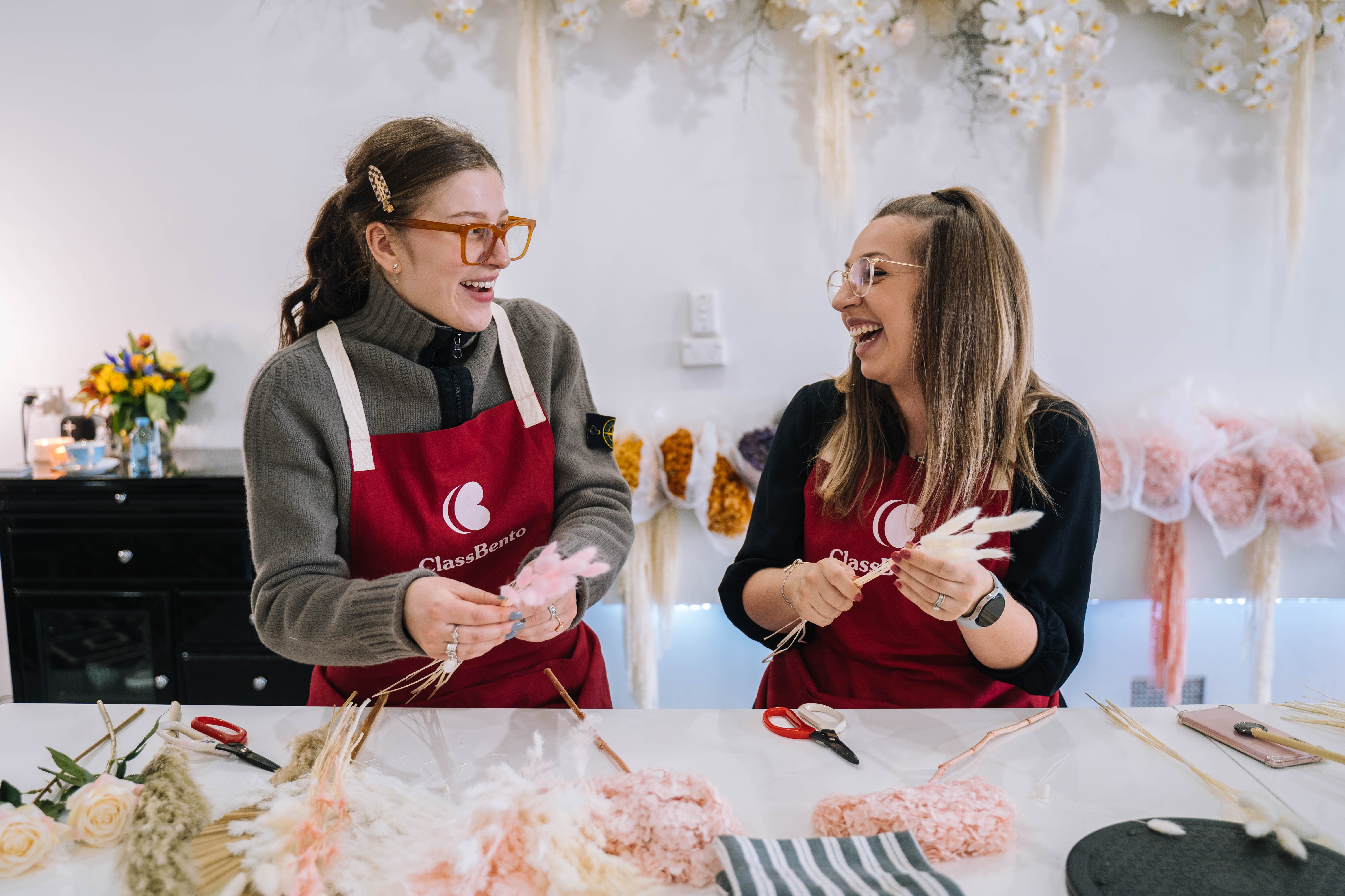 Two women are laughing and arranging flowers at a floristry class