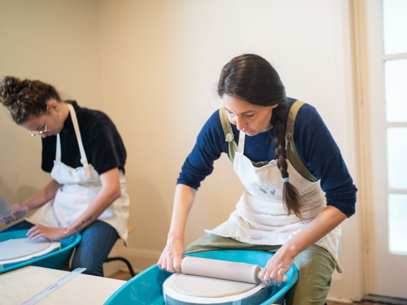 Two women rolling out clay for a pottery wheel class