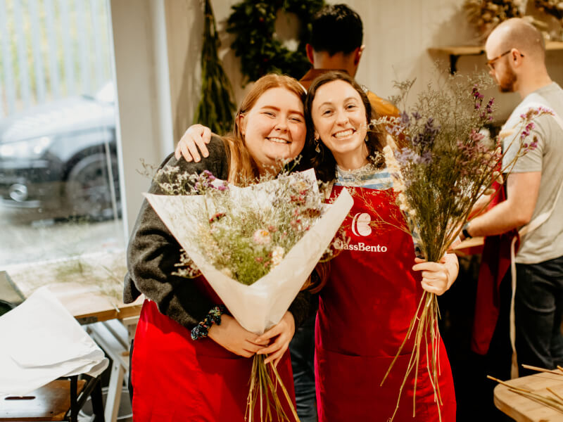 Two women smiling and posing with their bunches of flowers