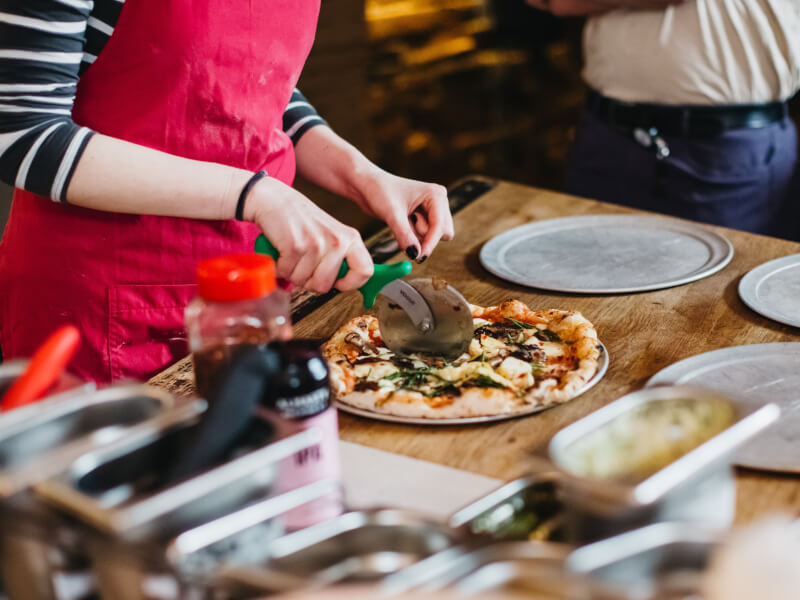 A close upshot of a person using a pizza wheel to cut a homemade pizza into slices