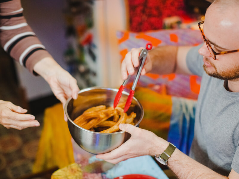 A person is taking a churro out of a saucepan with a pair of red tongs