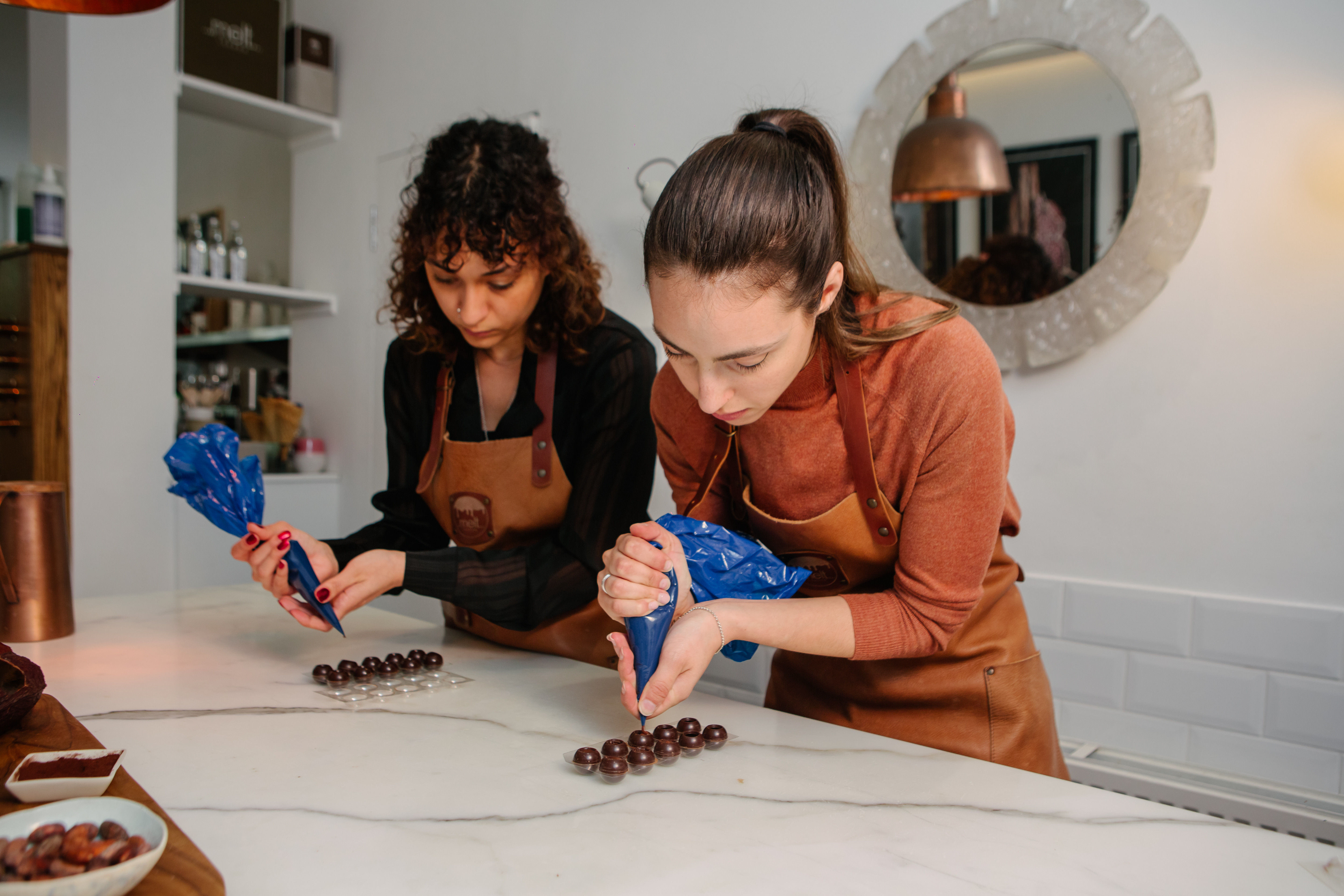 Two women are piping the fillings into handmade chocolate truffles