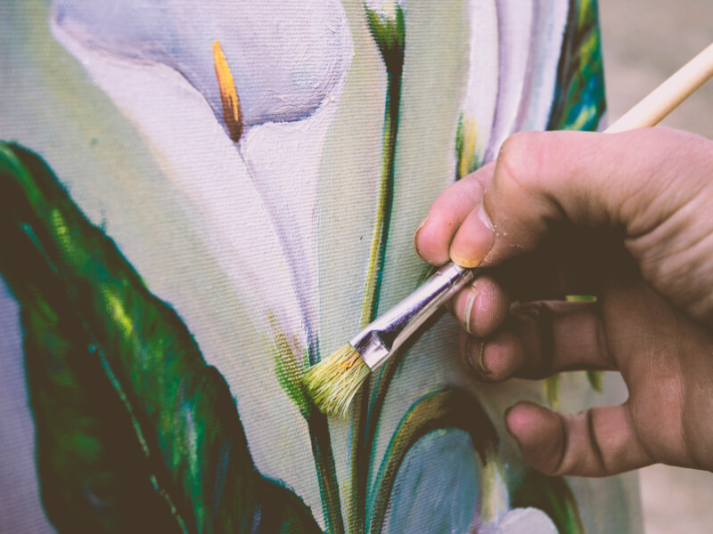 A person painting a flower on an art canvas using a paintbrush