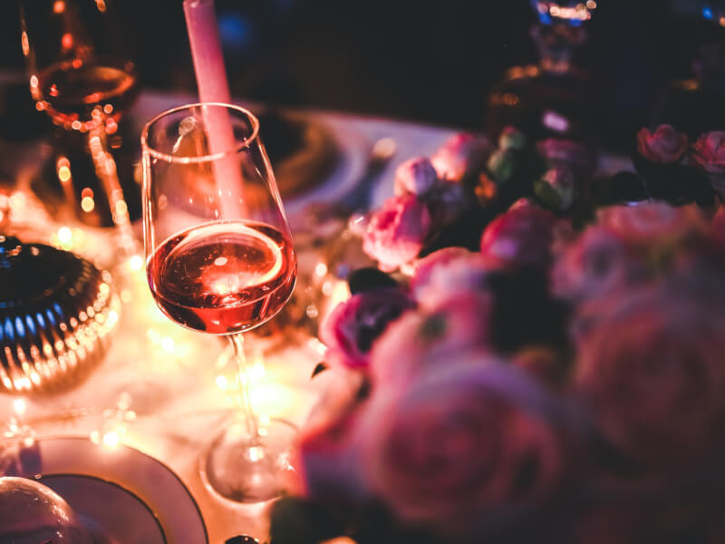 A tall wine glass on a table decorated with pink flowers and lights