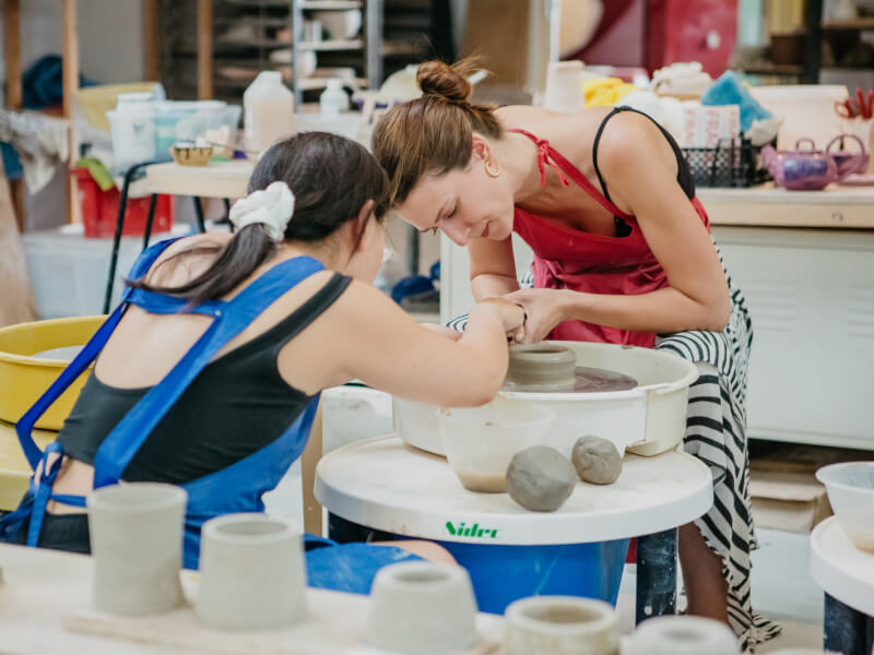 Two women are making a pot on a wheel at a pottery workshop