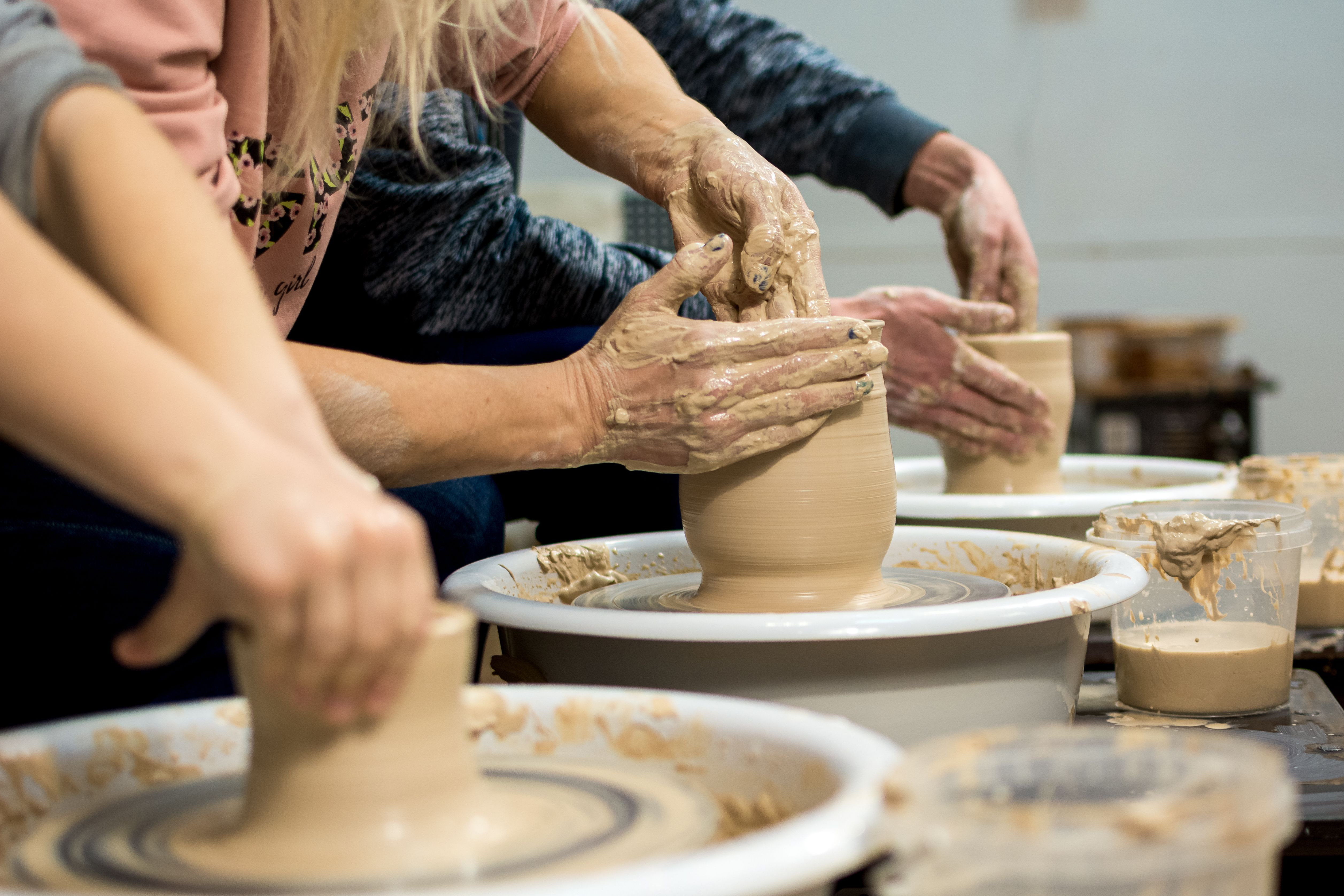 A close up of three peoples hands working with clay on pottery wheels