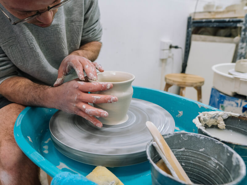 A close up of a man making a clay pot on pottery wheel