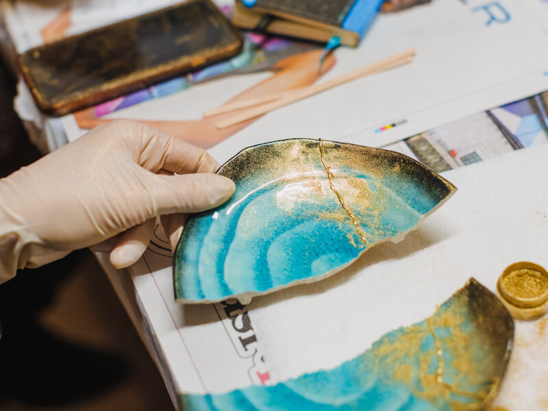 A person is using gold resin powder and resin to repair a broken plate at a kintsugi class