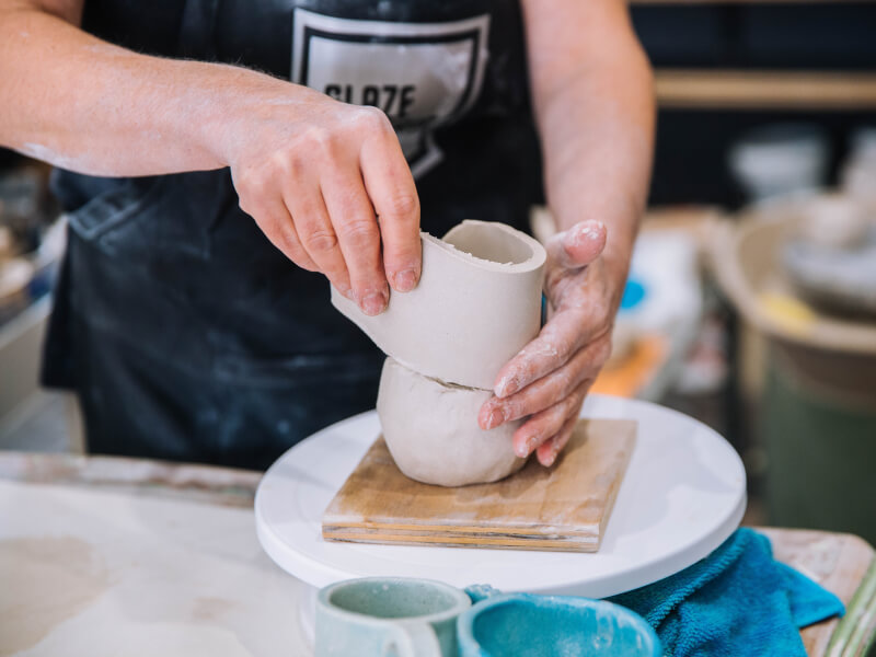 A person is using slab building techniques to make a pot from clay