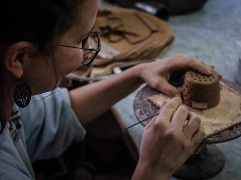 A lady uses a tool to work on some hand-built pottery