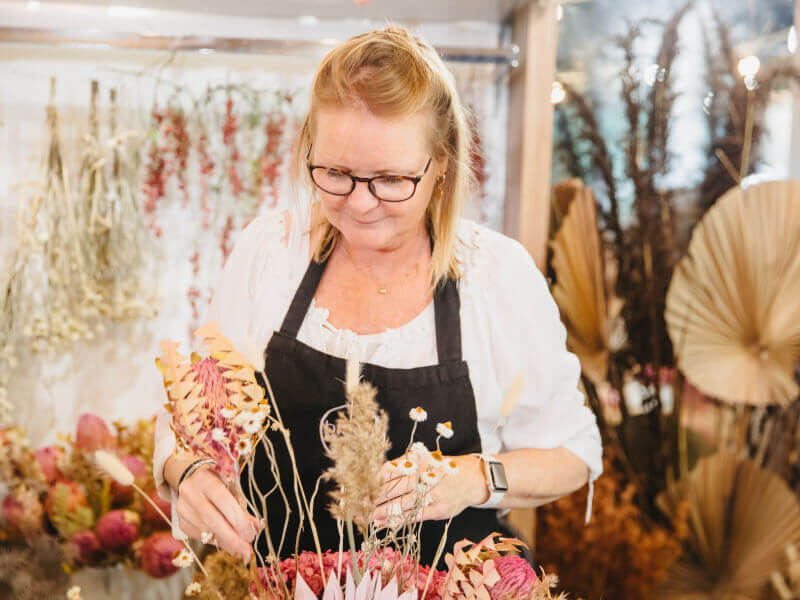 A woman is arranging dried flowers in a vase