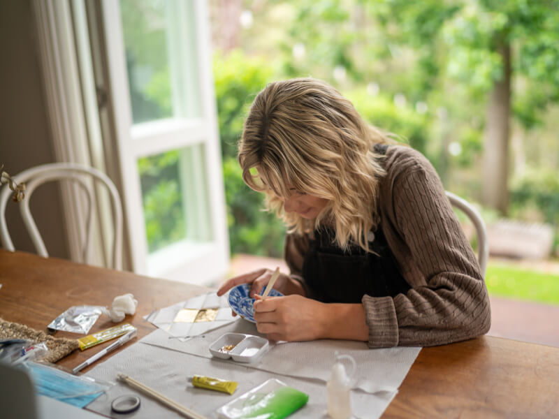 A woman is sitting at a table working on a small kintsugi bowl