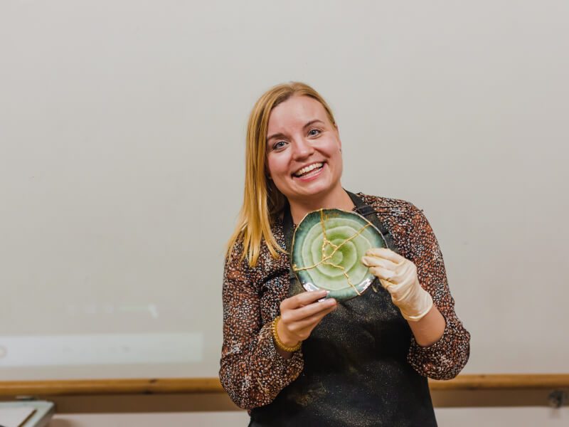 A woman is holding a finished kintsugi plate and smiling