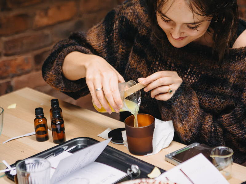 A woman is pouring melted wax into a container to make a candle