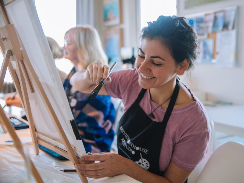 A woman is sitting at an easel, painting
