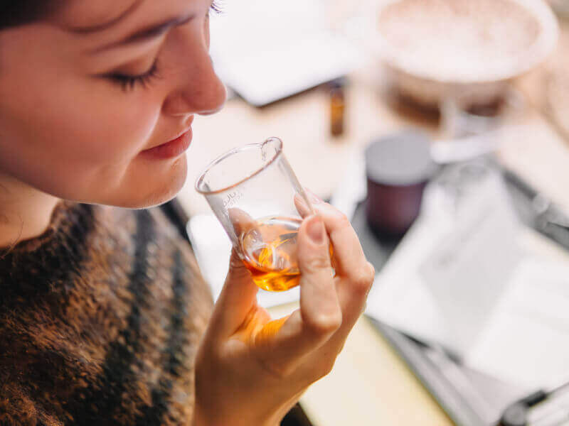 A woman is smelling a glass beaker filled with essential oils