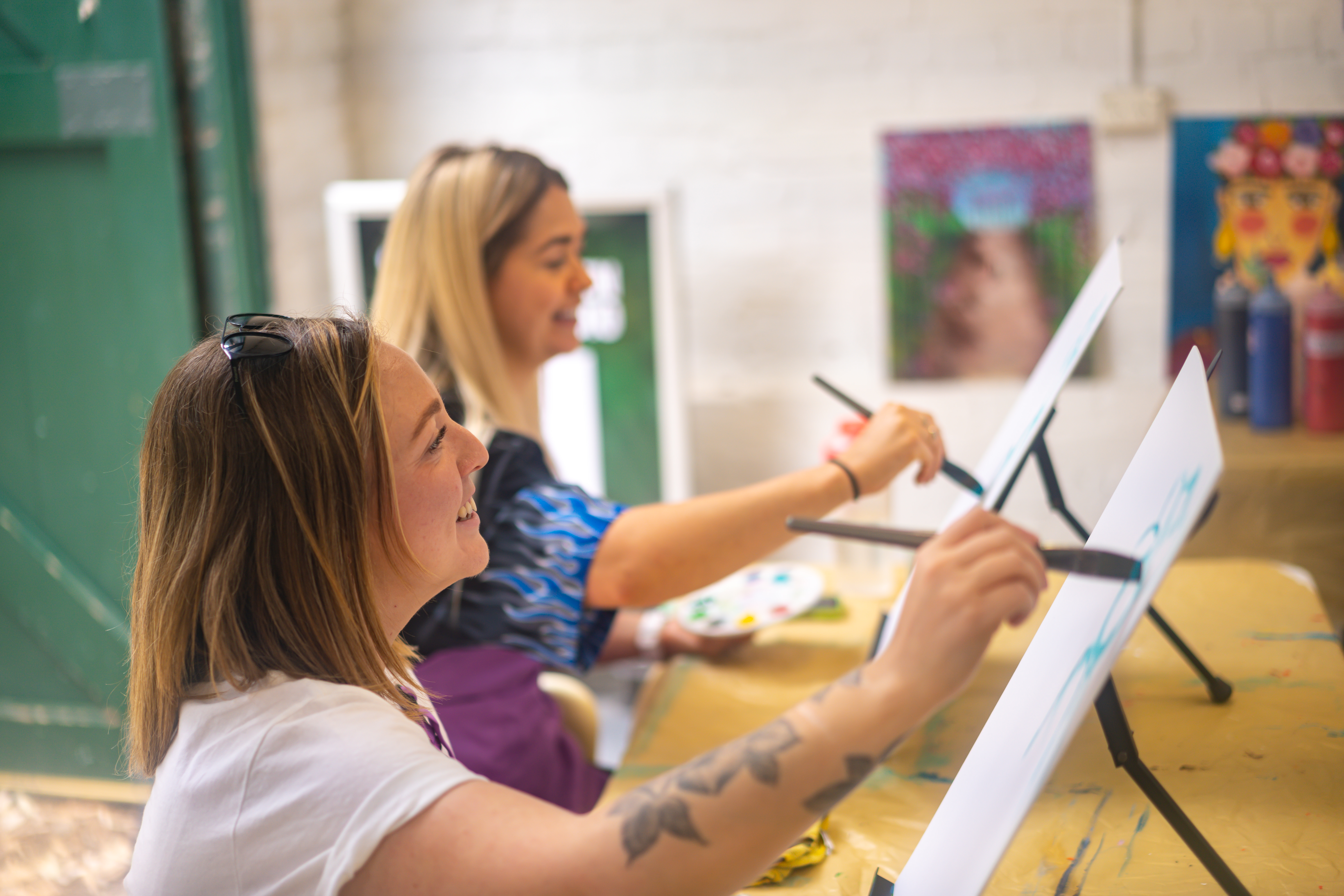 Two women sitting at easels at a paint and sip class