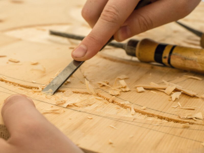 A close up of a person using a chisel to cut a section out of a piece of wood