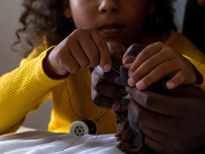 Young girl in a yellow sweater helping her parent with sewing